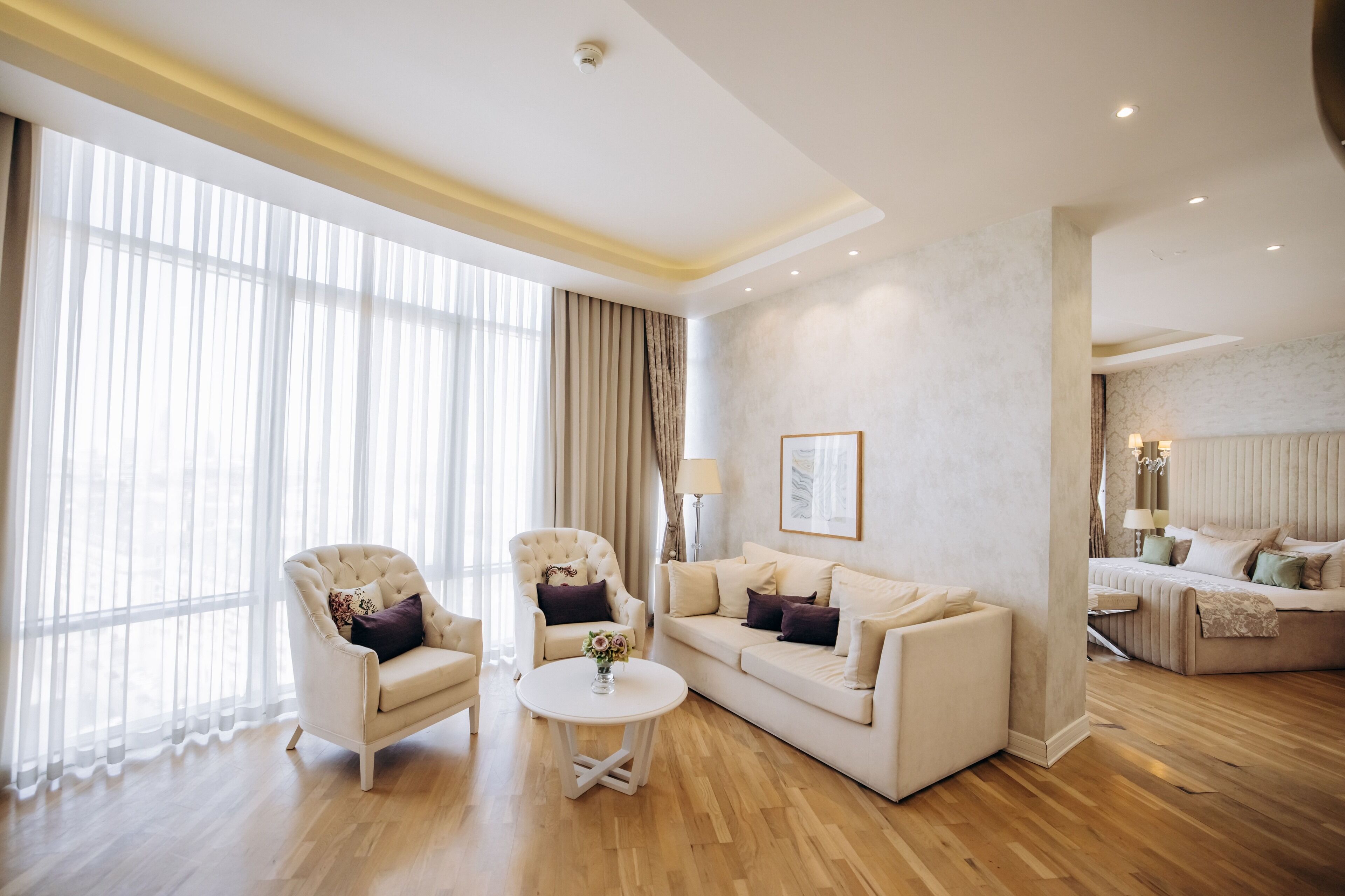 A spacious living room with a large window, a sofa set, a coffee table, and a separate seating area with a lamp.