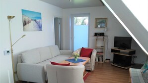 A living room with a sofa, a coffee table, and a television. There is a bookshelf and a painting on the wall.