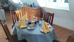 A dining table set with a blue tablecloth, wooden chairs, and a fruit basket.