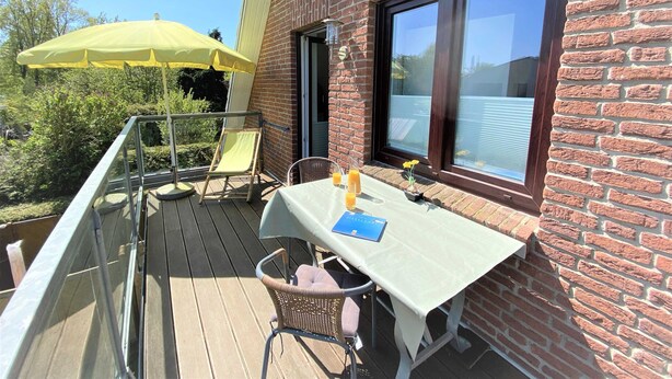 A balcony with a table, chairs, and a yellow umbrella.