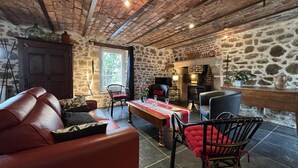 Une pièce rustique avec un mur en pierre, une cheminée, un canapé en cuir et une table à manger agrémentée d’un chemin de table rouge.