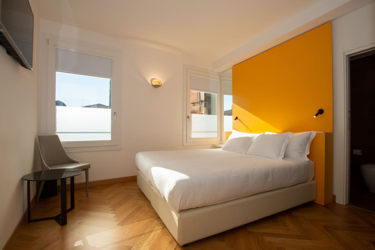 Un dormitorio con una cama, una silla, una mesa y un ventanal.