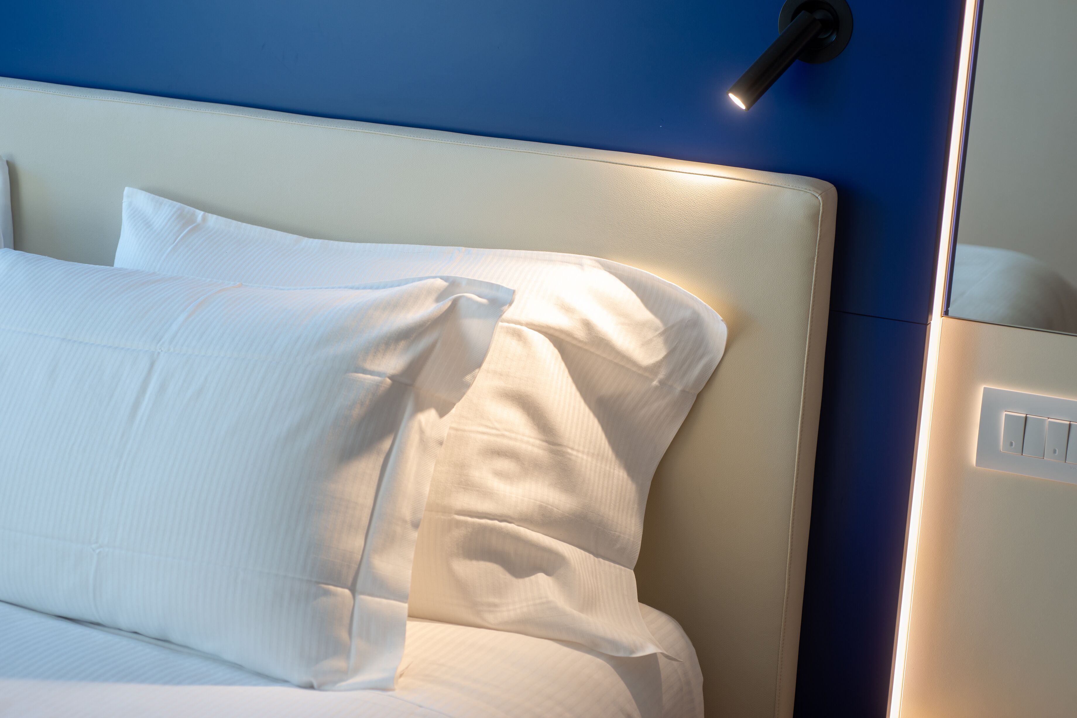 Un letto rifatto con lenzuola bianche e una testiera, su una parete blu.