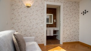 A modern room with a patterned wallpaper, a wooden floor, a white sofa, and a bathroom visible through an open door. - Padova Suites C20 (Padova)