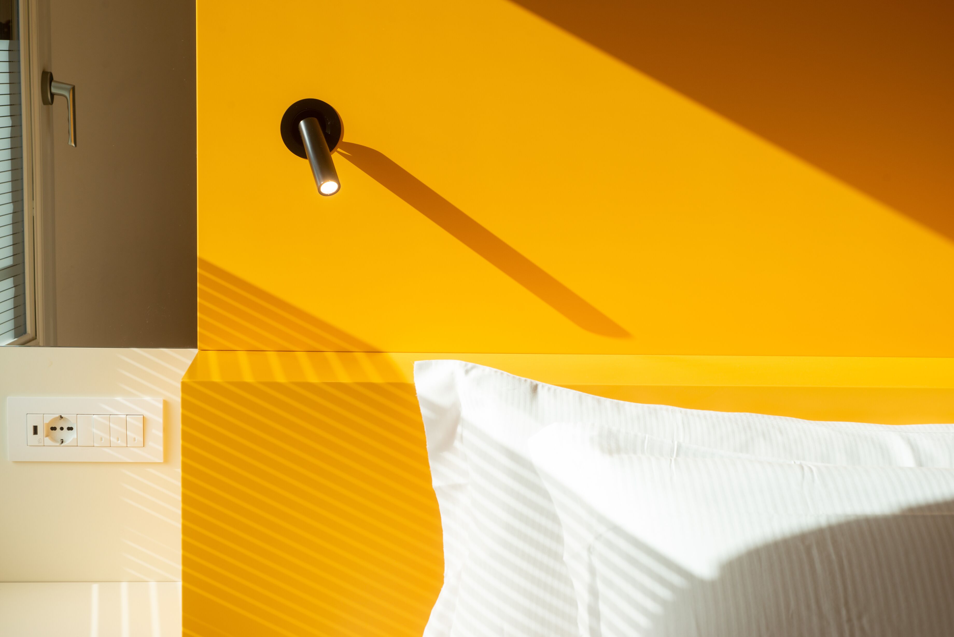 A room with a yellow wall, a white door, a light switch, and a white pillow.