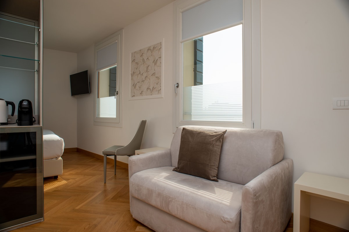 Una sala de estar moderna con un sofá, una silla, un televisor de pantalla plana montado en la pared y una ventana con persianas.