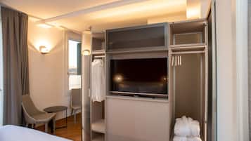 Une chambre d’hôtel comprenant un lit, un coin salon avec des fauteuils, une télévision, une armoire et une fenêtre avec des rideaux.
