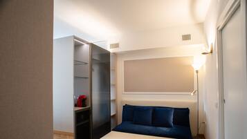 Um quarto com uma cama, um banco branco, um guarda-roupa e um abajur.
