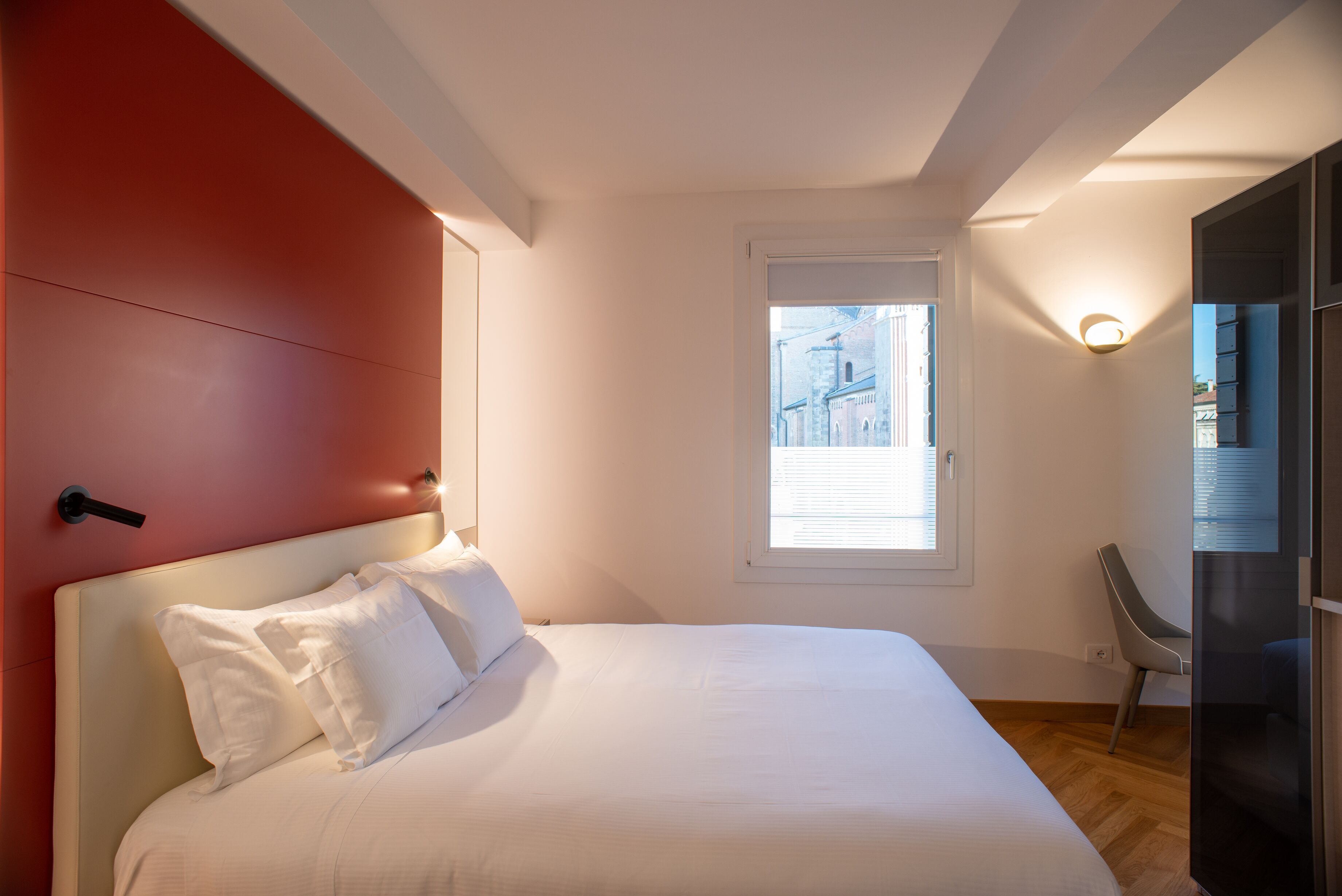 A bedroom with a bed, a window, a chair, and a door.