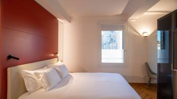 A bedroom with a bed, a window, a chair, and a door.