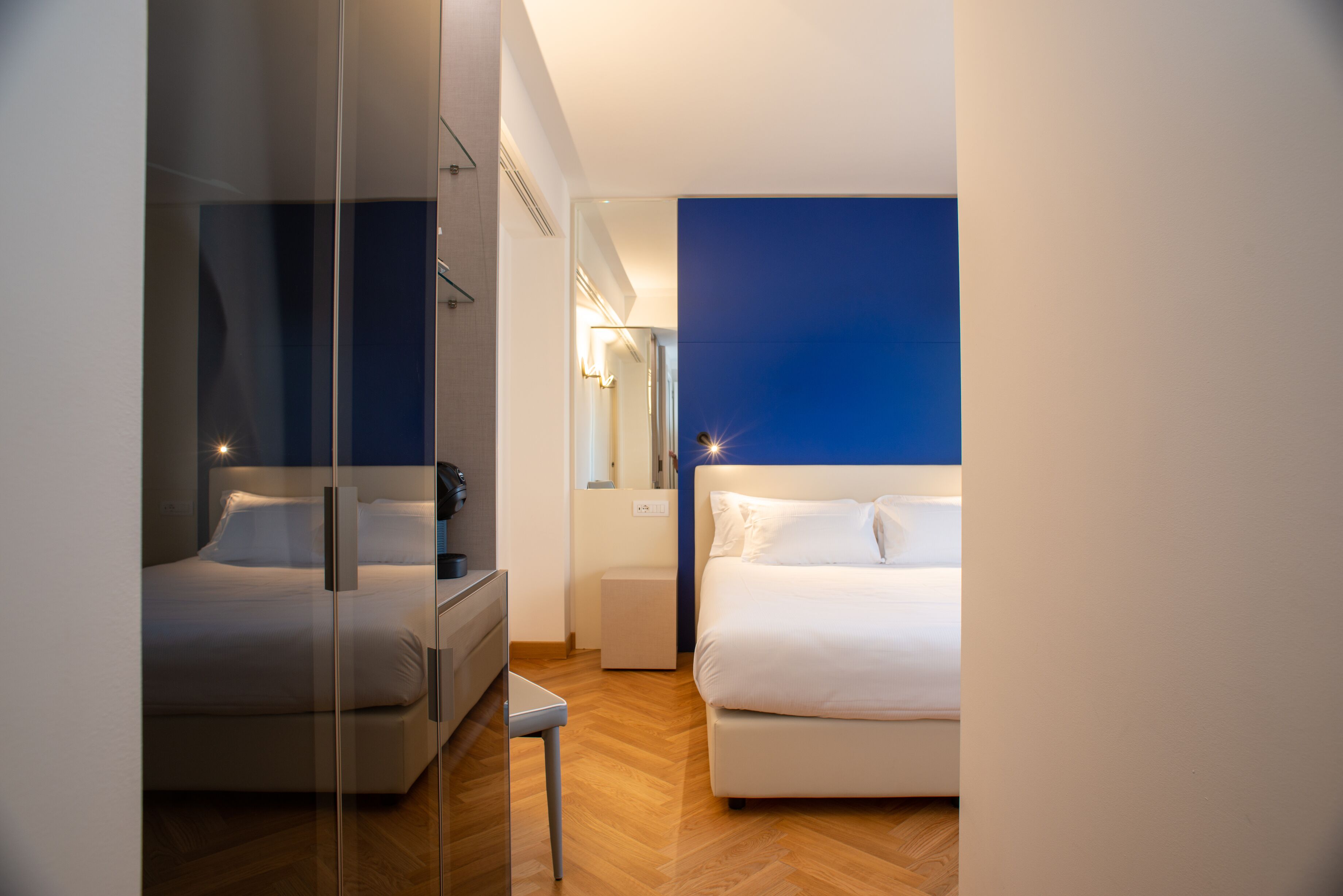 A modern hotel room with a glass partition, a bed, a bedside table, and a nightstand.