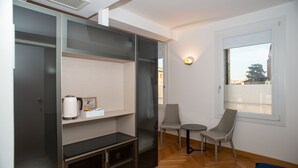 A compact room with a built-in wardrobe, a small table, two chairs, and a window with blinds. - Padova Suites C20 (Padova)