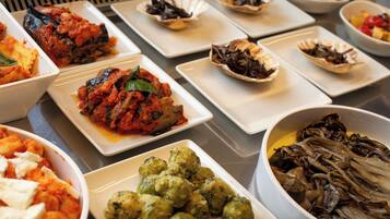 Buffet com diversos pratos, incluindo legumes assados, massas e saladas.