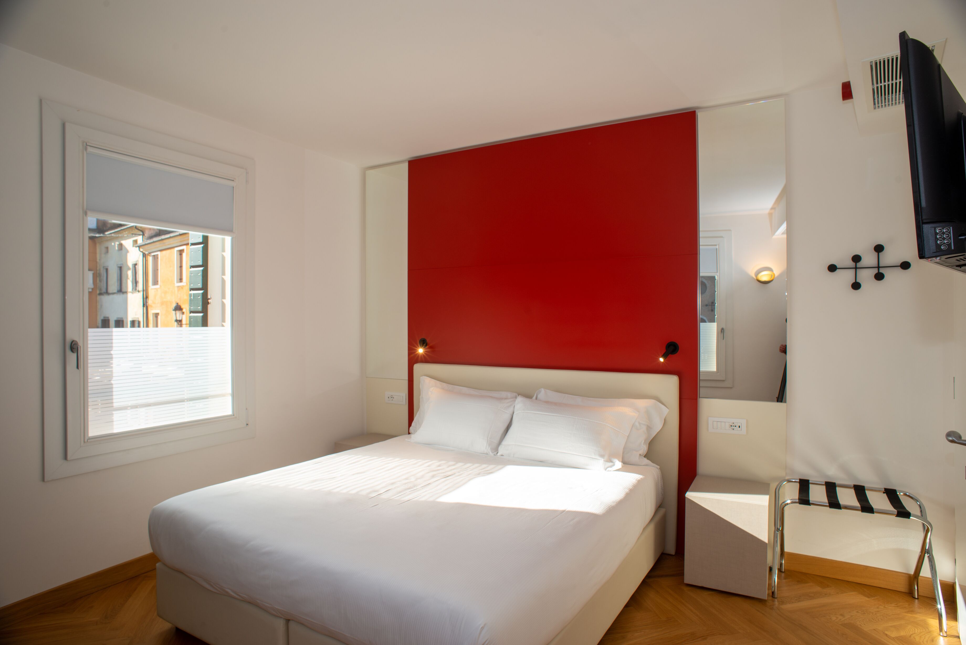 A bedroom with a large bed, a red accent wall, a small bedside table, and a chair.