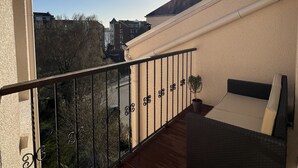 Un balcone con pavimento in legno, ringhiera in metallo e vista su edifici e alberi sullo sfondo.