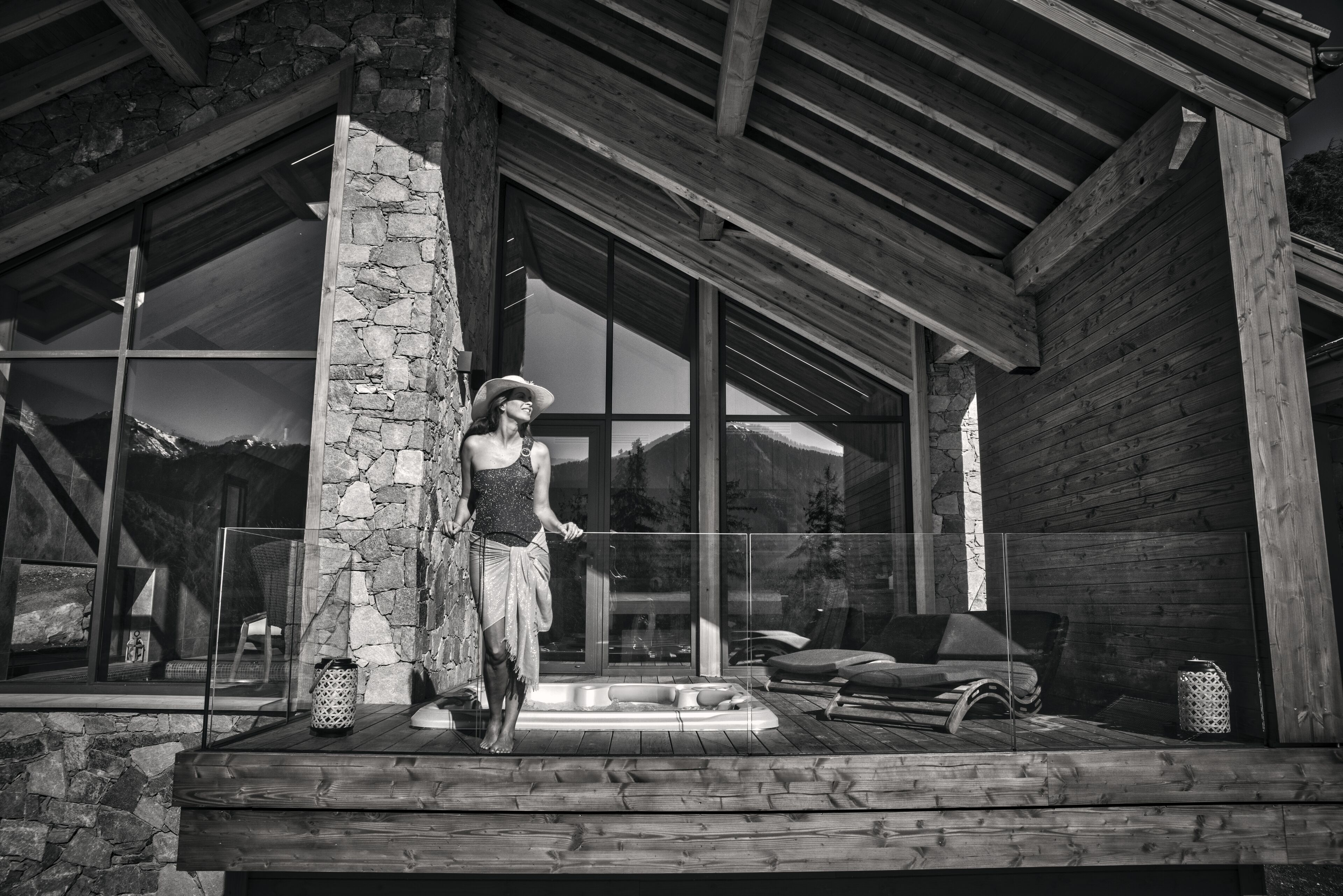 A wooden deck with a stone wall, a glass door, and a hot tub.