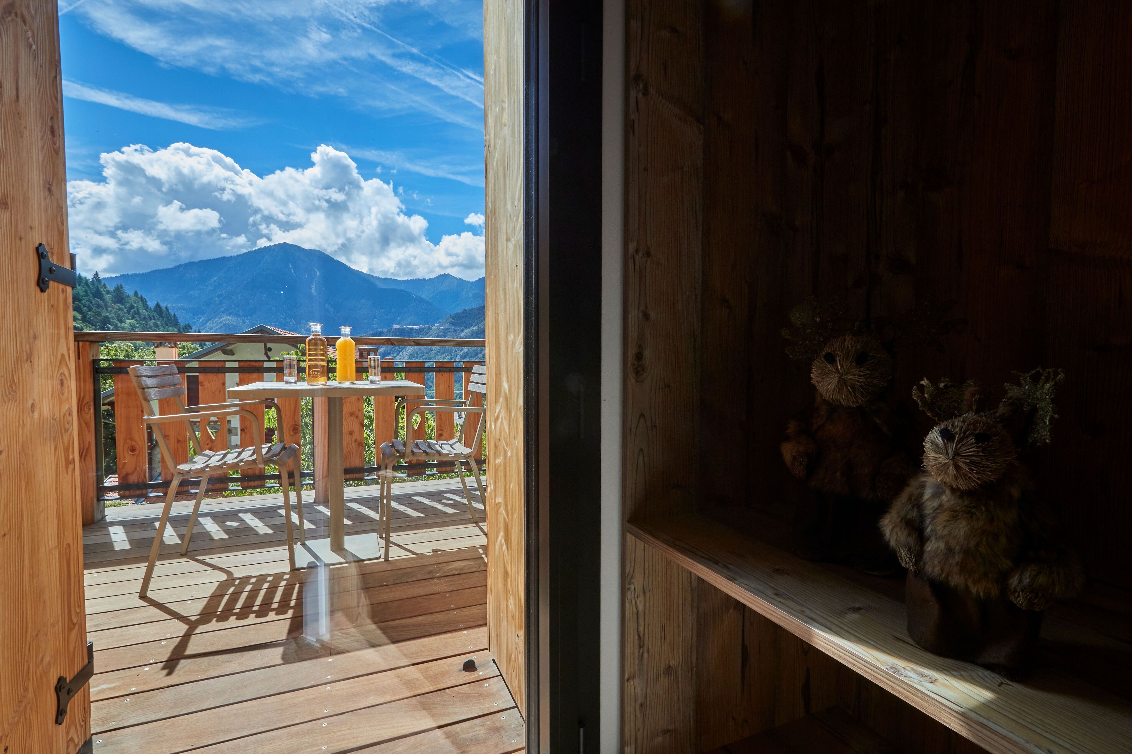 Una terraza de madera con una mesa y sillas, vista a la montaña, y un estante con adornos.