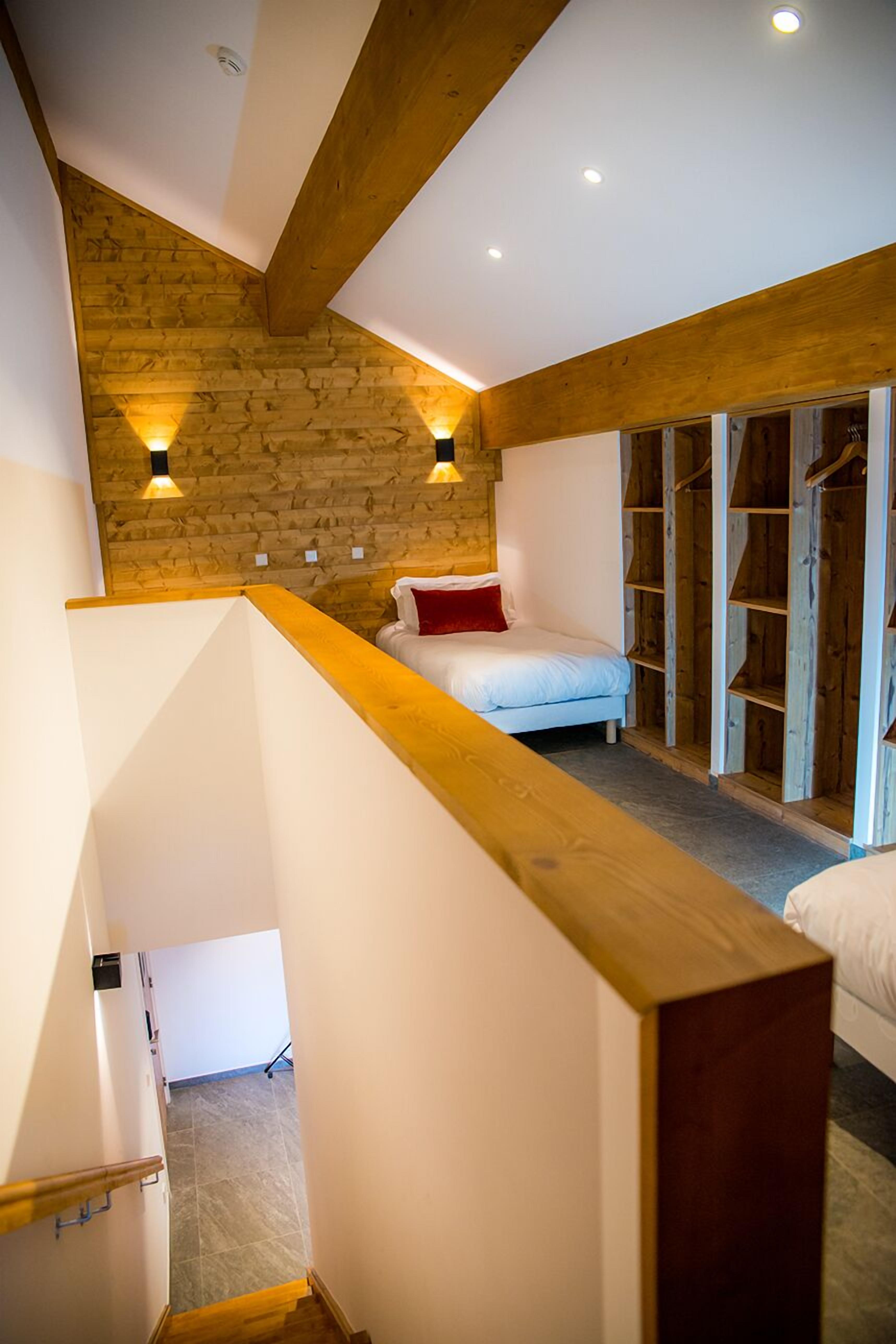 Une chambre avec un plafond en pente, un lit avec un oreiller rouge et une armoire en bois.