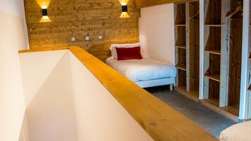 Une chambre avec un plafond en pente, un lit avec un oreiller rouge et une armoire en bois.