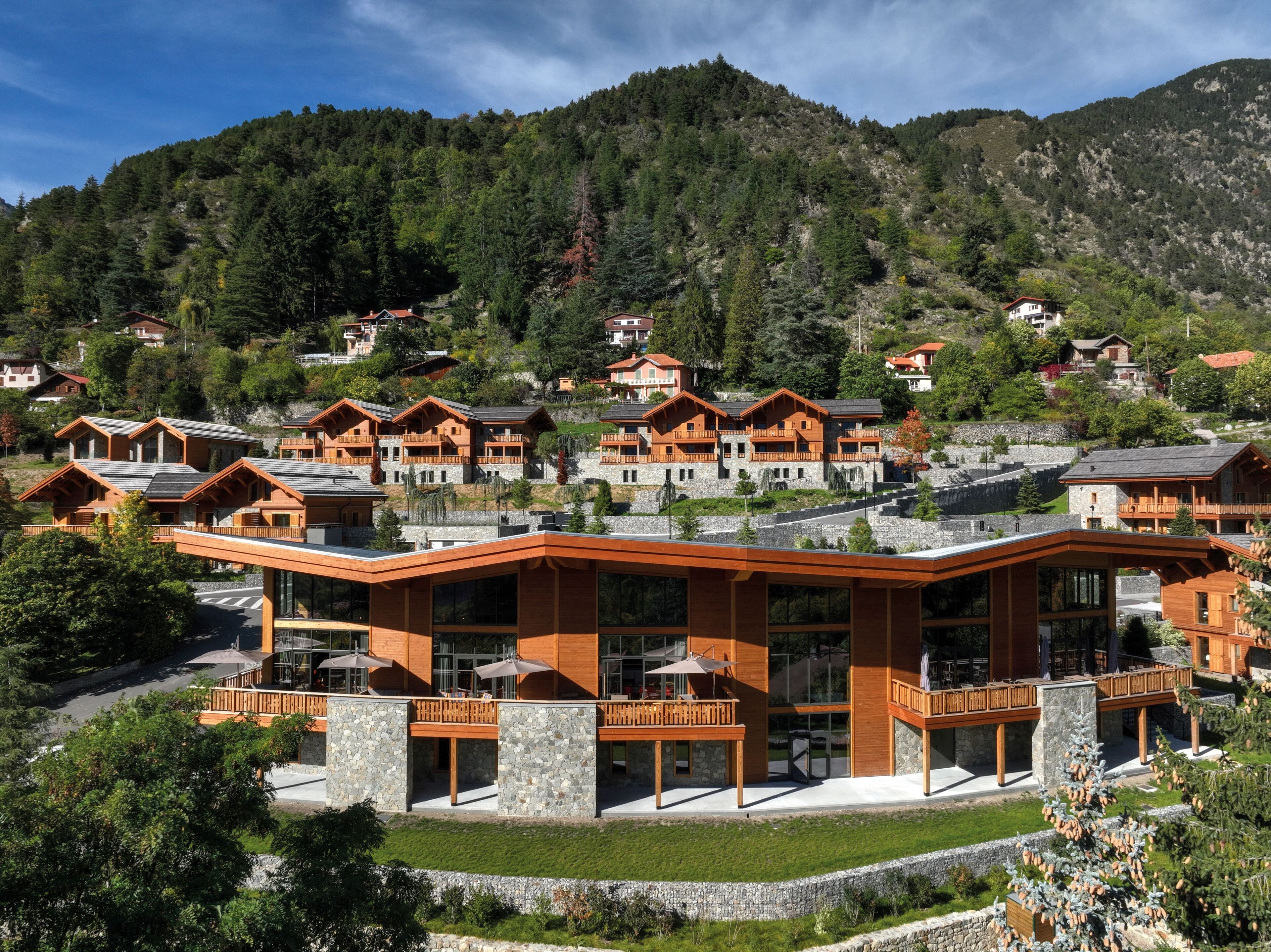 Un complexe hôtelier moderne doté de chalets en bois et d’un bâtiment principal avec de grandes fenêtres et un espace de détente extérieur.