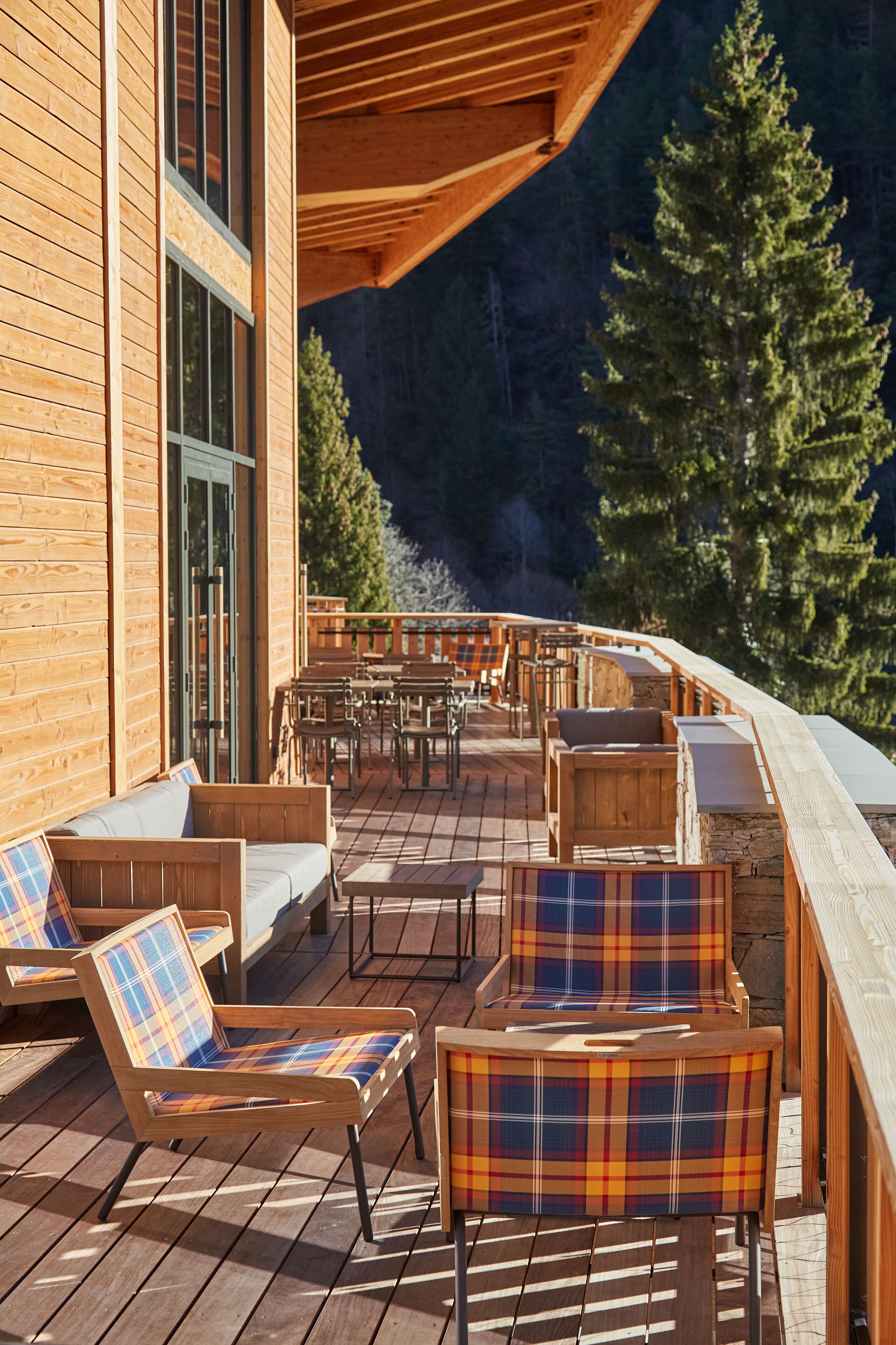 A wooden deck with outdoor seating, including chairs and a sofa, overlooking a forested area.