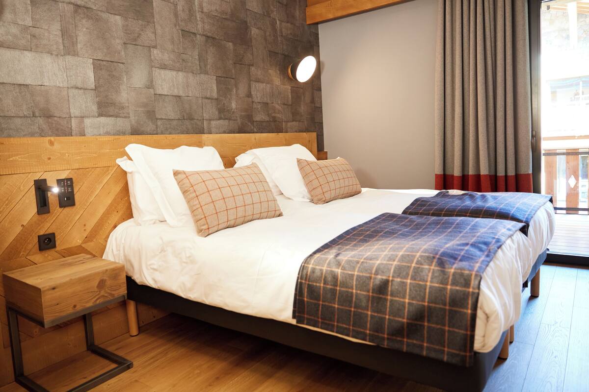 A double bed with a plaid blanket, a wooden headboard, and a nightstand with a lamp.