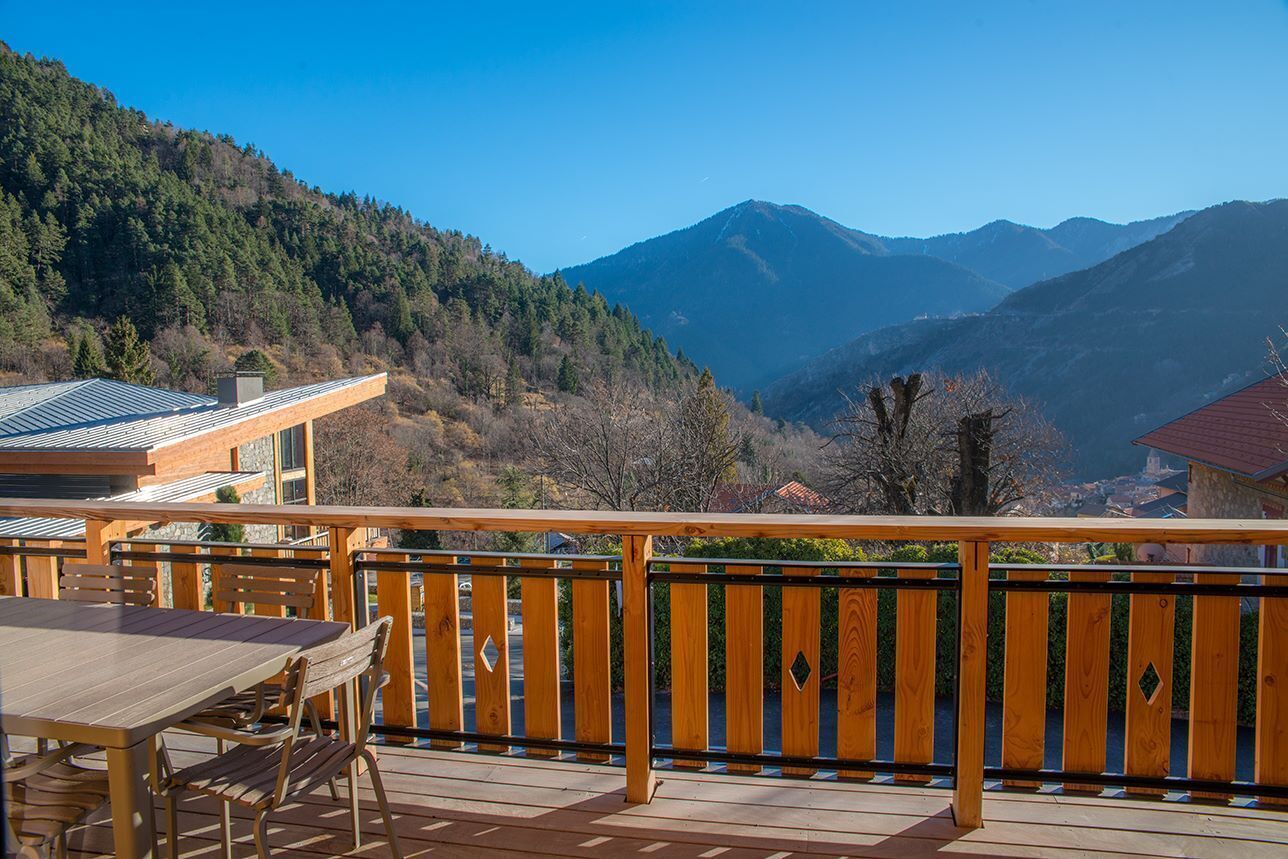 A wooden deck with a table and chairs, overlooking a mountainous landscape.