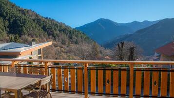 A wooden deck with a table and chairs, overlooking a mountainous landscape.