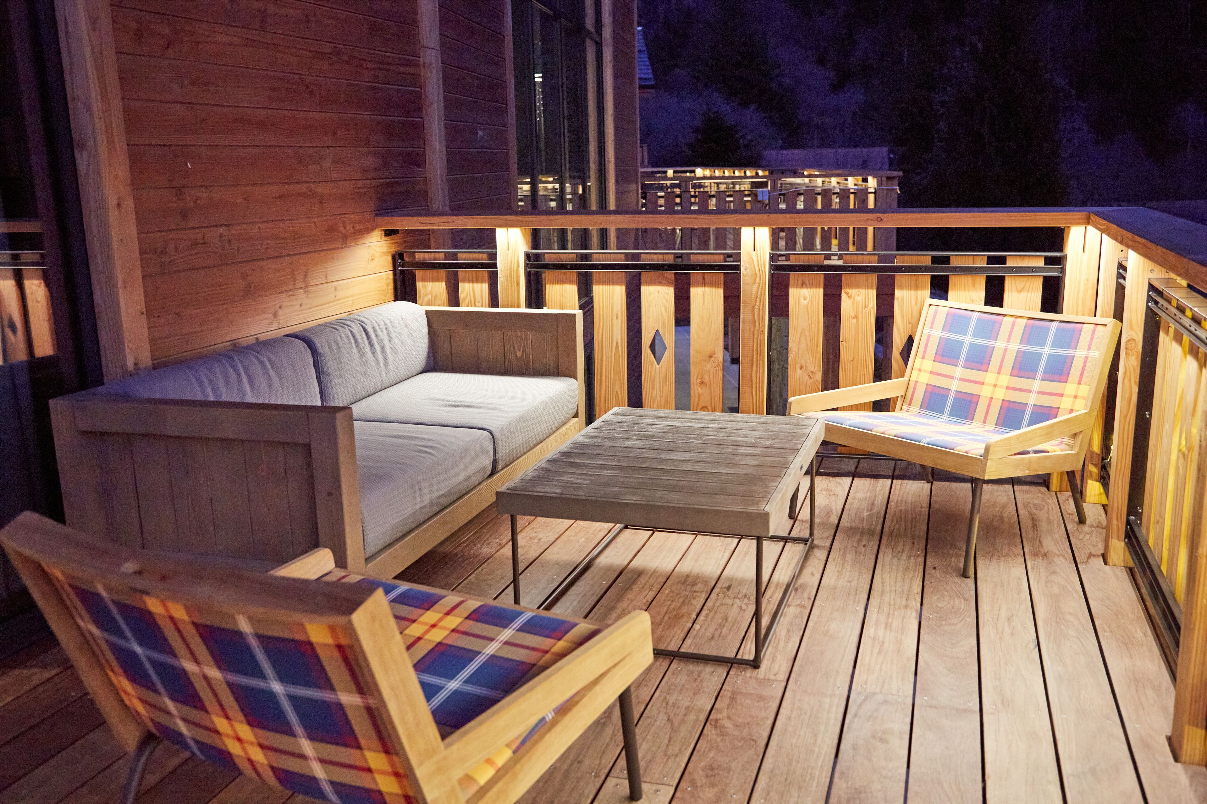 A wooden deck with a sofa, two plaid chairs, and a small table.