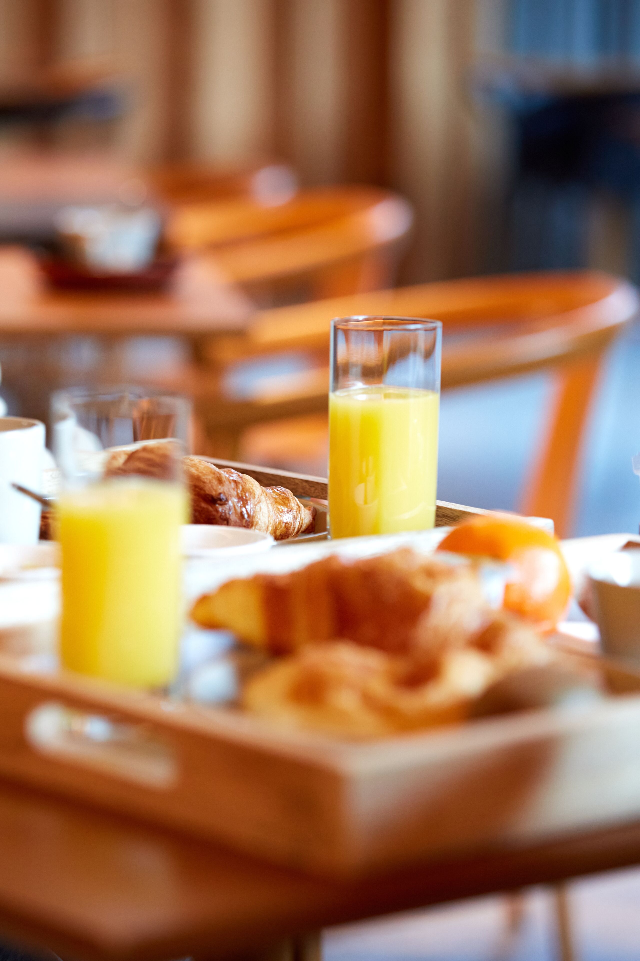 Een ontbijtplateau met croissants en sinaasappelsap op een houten tafel in een eetruimte.