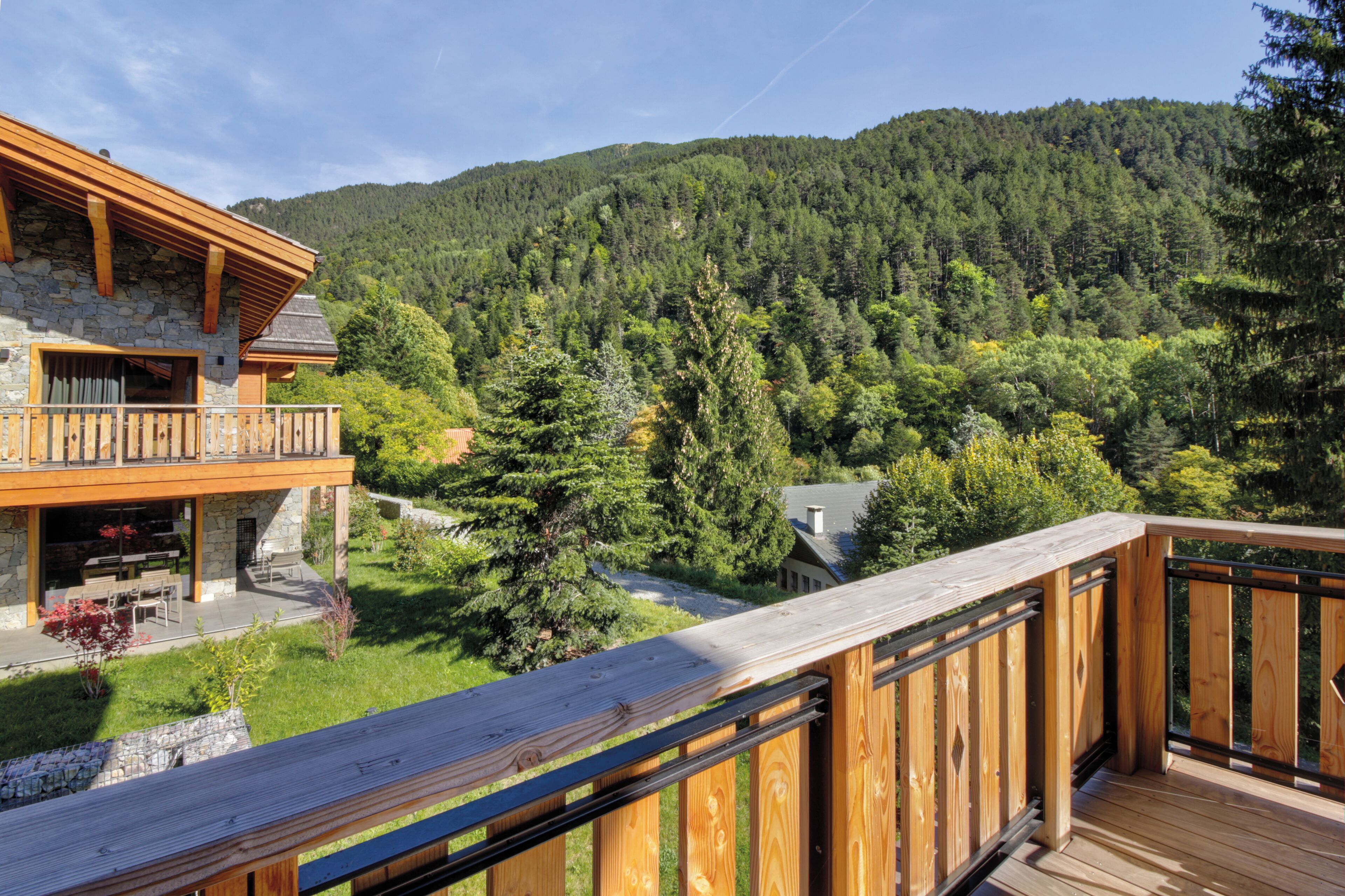 A wooden deck with a stone building in the background, surrounded by a forested hillside.