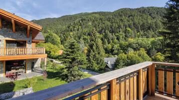 A wooden deck with a stone building in the background, surrounded by a forested hillside.