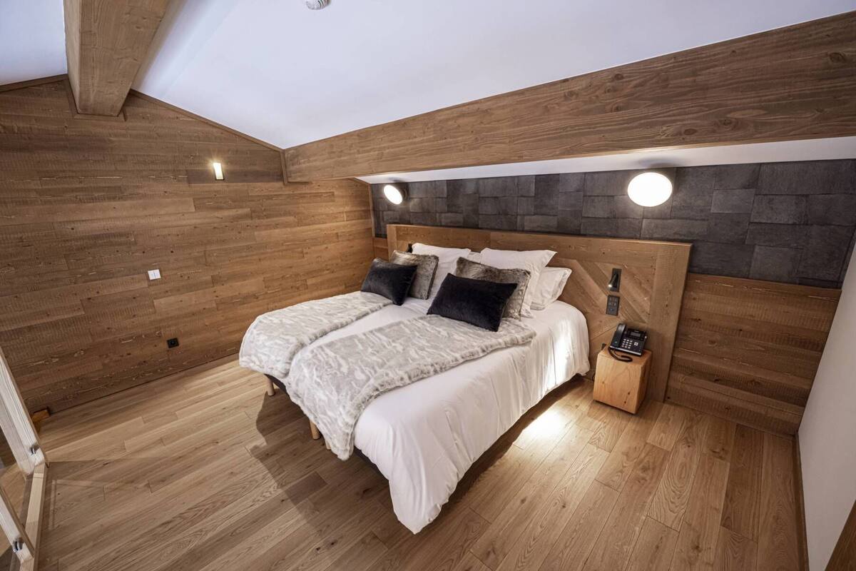 A bedroom with a wooden headboard, two beds, a bedside phone, and a stone wall.