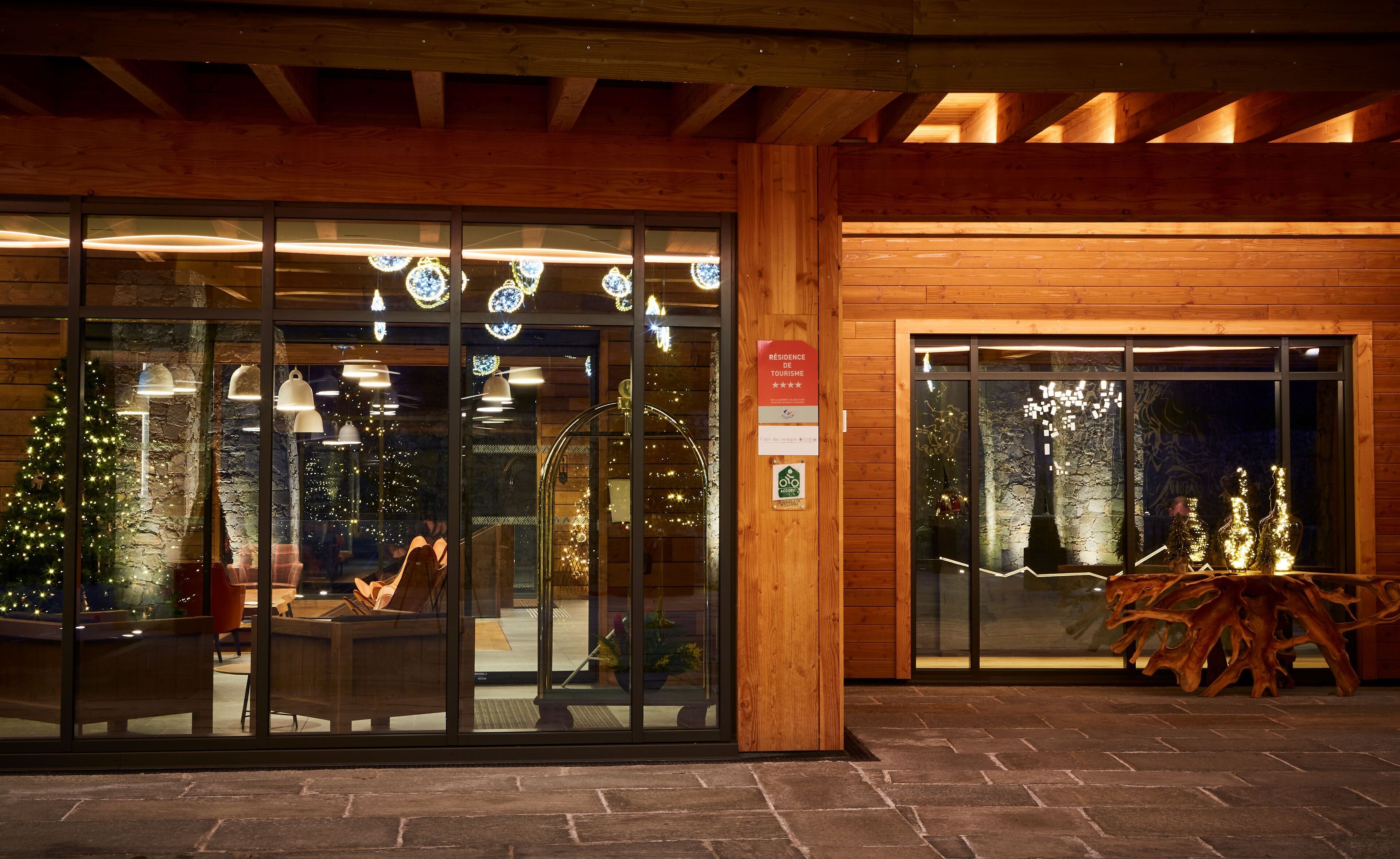Fachada de madera con grandes puertas de cristal, un árbol de Navidad en el interior y un cartel que indica una calificación de 4 estrellas.