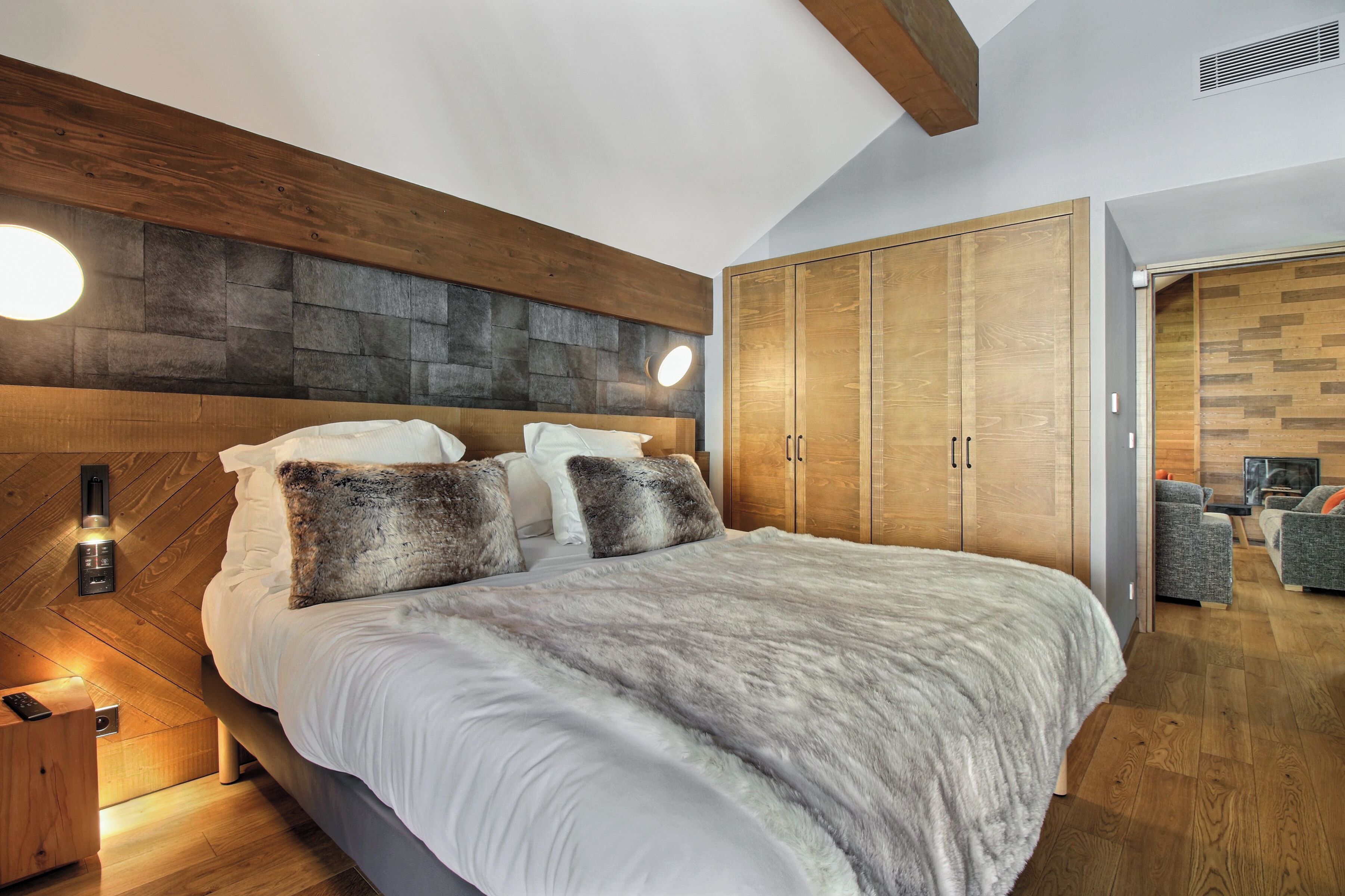 Une chambre moderne avec un grand lit, une tête de lit en bois et une armoire intégrée.