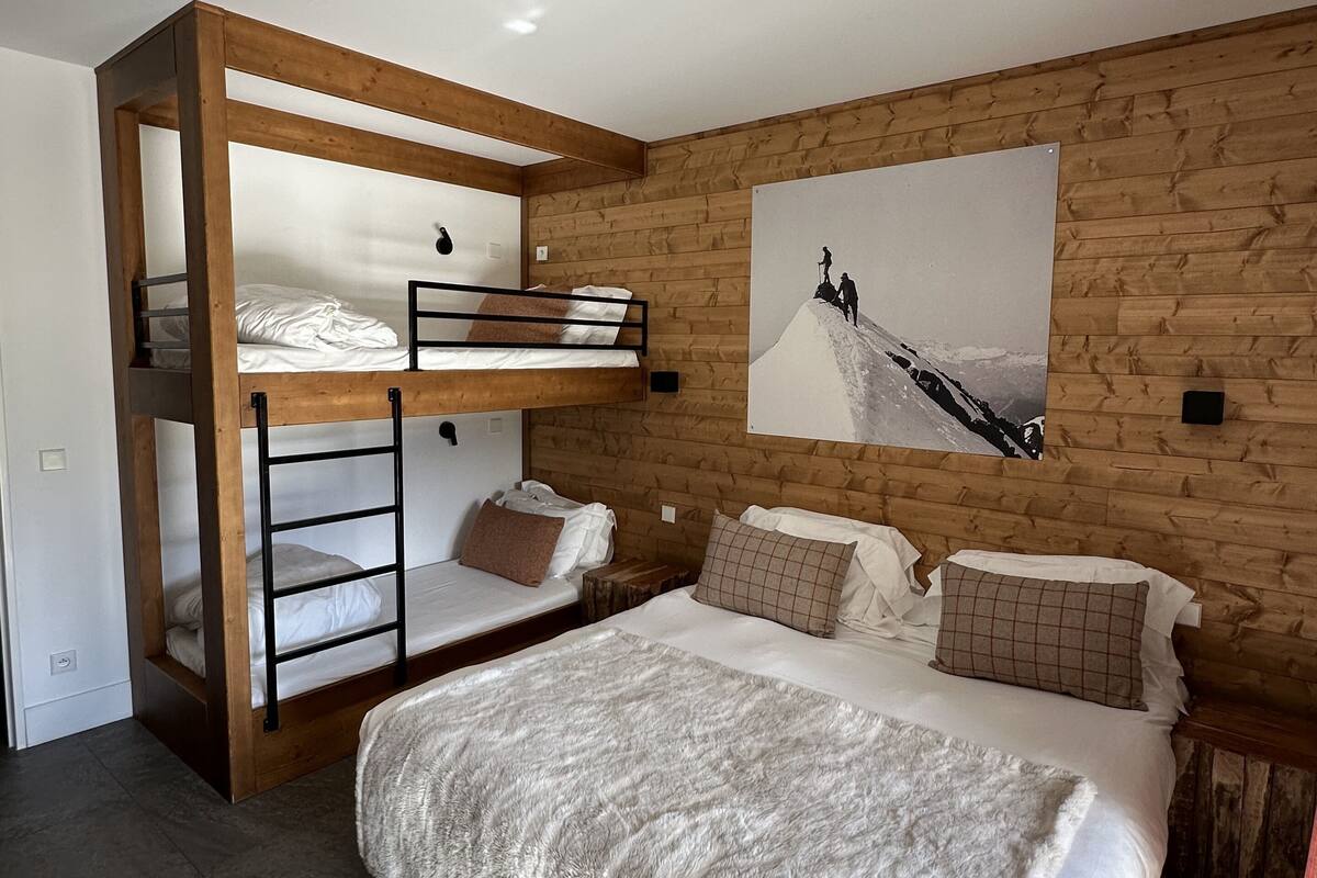 A bedroom with a bunk bed, a large bed, and a wooden wall.