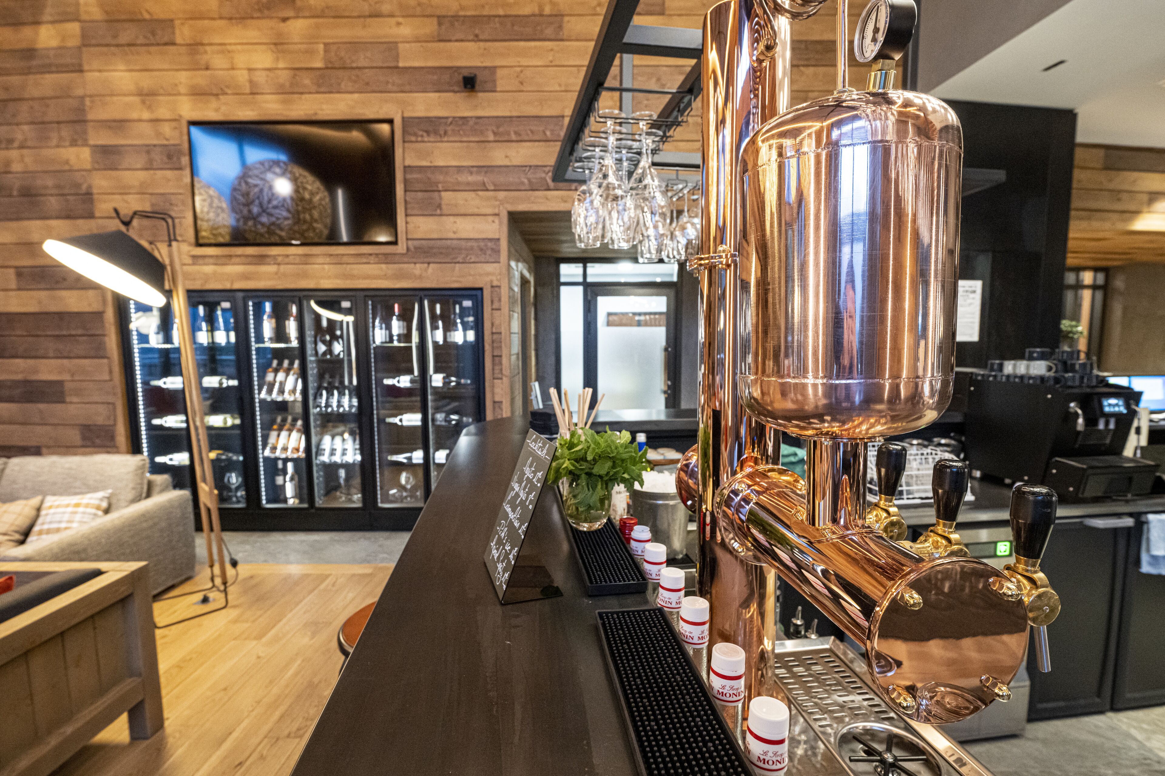 Un espace bar doté d’un système de robinets à bière en cuivre, d’un comptoir et d’un coin salon avec un canapé et un téléviseur.