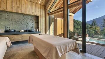A spa room with a massage table, wooden paneling, a stone wall, and a view of a hot tub and mountains.