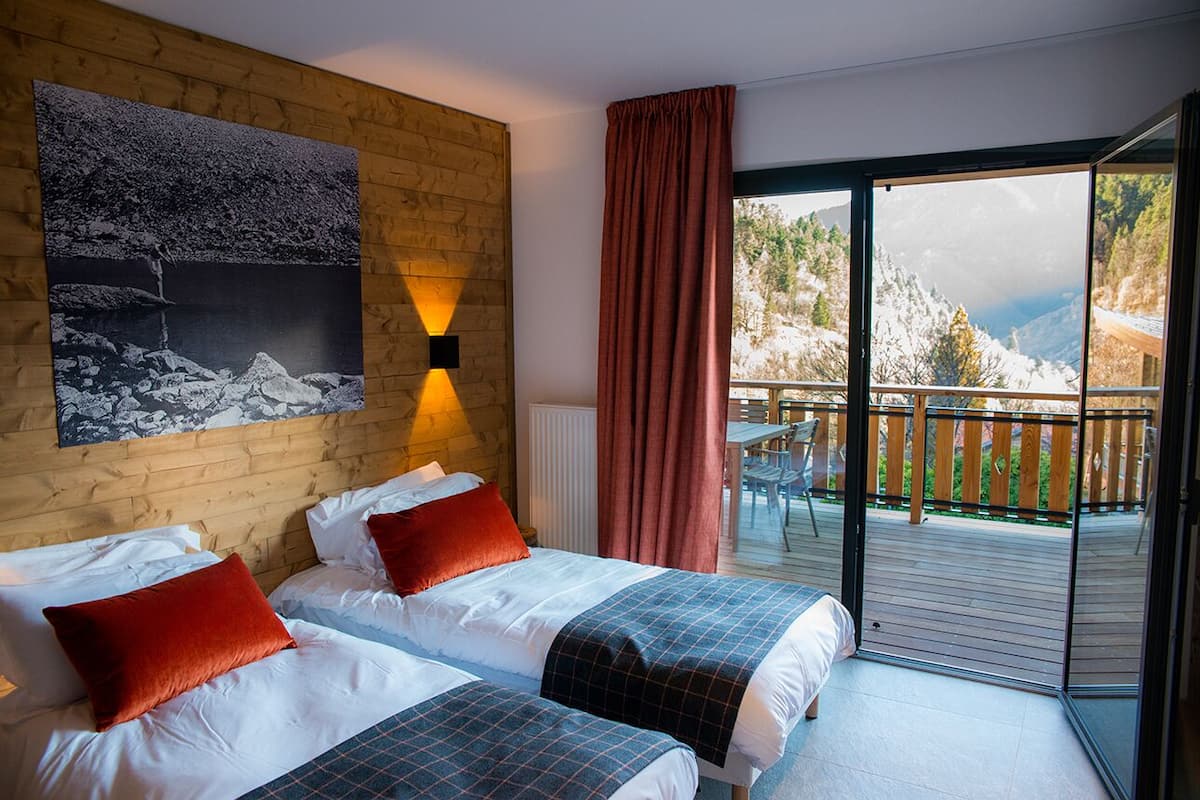 A hotel room with two beds, a large window with a view of a mountain, and a wooden wall with a painting.