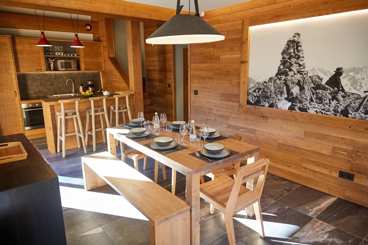 A modern kitchen with wooden cabinetry, a dining area with a long table set for six, and a large framed picture on the wall.