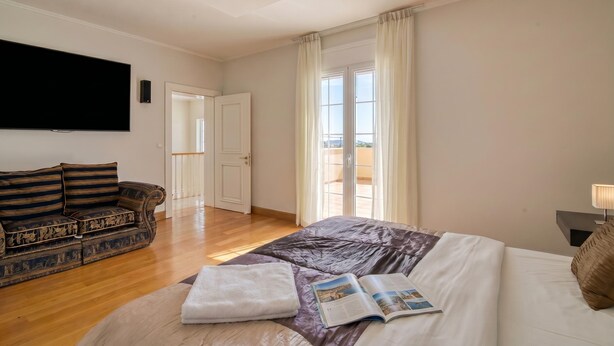A hotel room with a bed, a sofa, a flat-screen TV, a window with curtains, and a balcony. - Amazing Pool Villa Kyllini Sea View (Andravida-Kyllini)