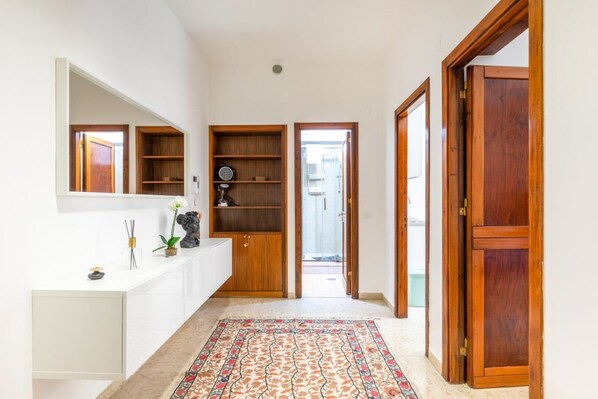 Un pasillo con una consola blanca, estantes de madera, un tapete estampado y una puerta de madera.