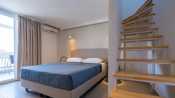 A modern hotel room with a bed, a staircase, and a view of the outdoors.