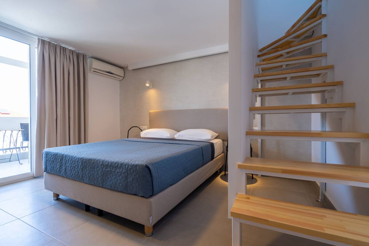 Quarto de hotel moderno com uma cama, uma escada e vista para o exterior.