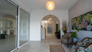 A spacious living area with a glass door leading to a balcony, a large floral painting on the wall, and a modern light fixture.