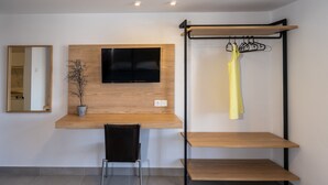 A modern room with a wooden desk, a mounted TV, a hanging clothes rack, and a potted plant.