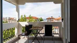 A balcony with a wooden table and two chairs, overlooking a coastal area with buildings and trees.