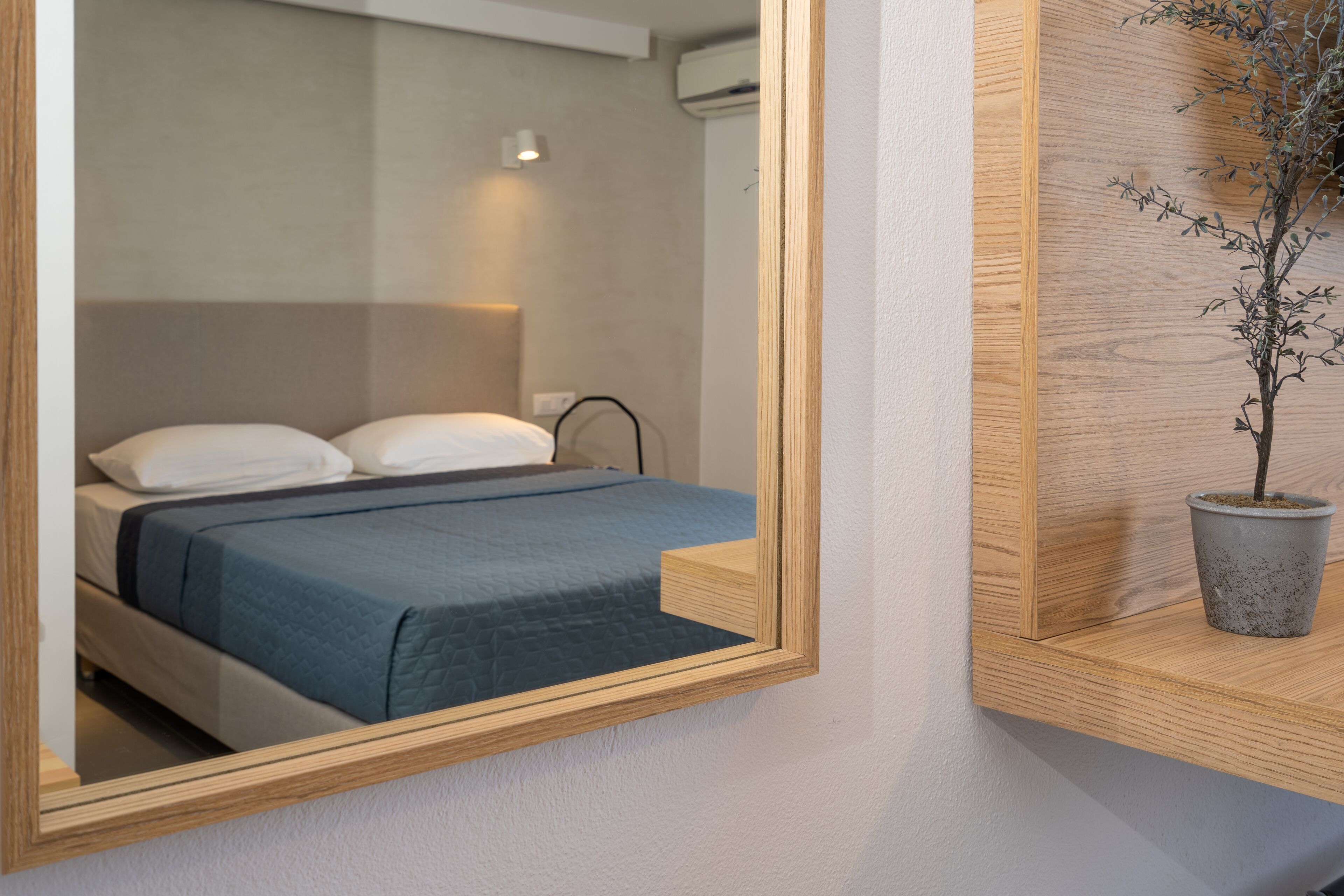 Un dormitorio moderno con cama, mesita de noche, planta en maceta y espejo.
