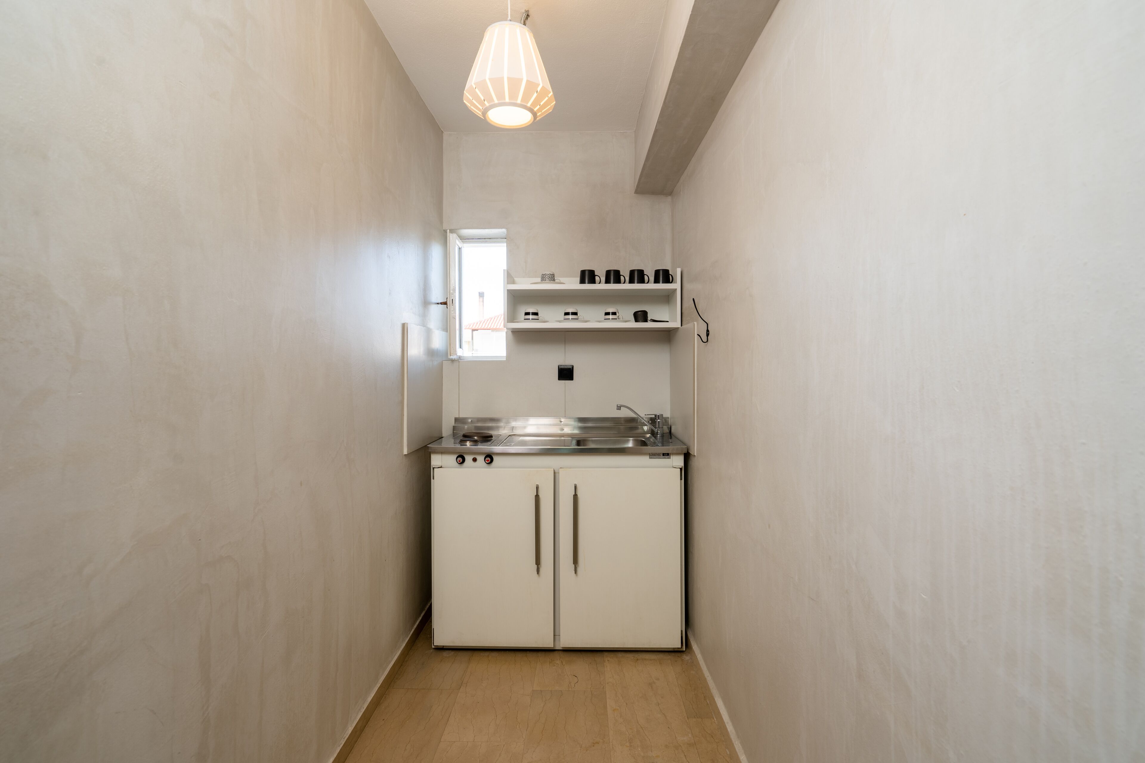 Una cocina estrecha con armarios blancos, una estufa de acero inoxidable y una lámpara colgante.