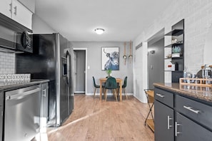 A modern kitchen with a dining area, featuring stainless steel appliances, a wooden dining table, and a brick wall.